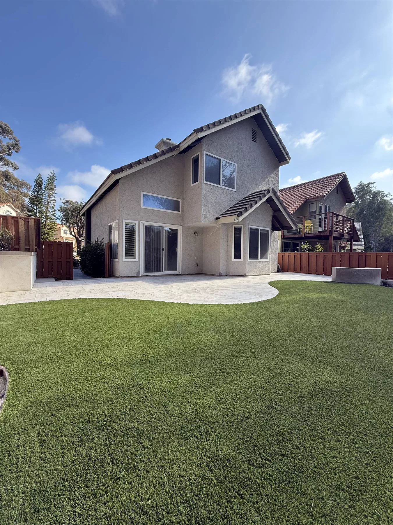 Finished Carlsbad backyard with curved premium artificial turf, porcelain pavers, retaining walls, and concrete transitions